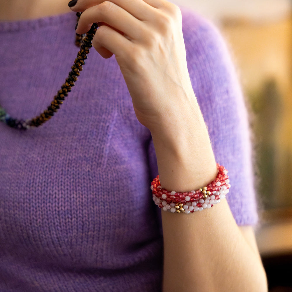 close up of handmade beaded gemstone bracelets in light and dark pink polka dots and gold worn on model