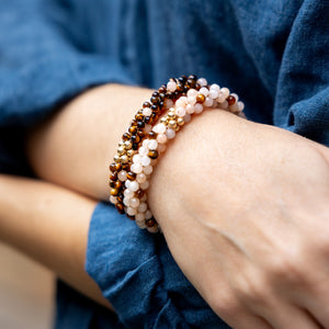 closeup of handmade beaded gemstone bracelets in brown and peach polka dots with gold worn on model