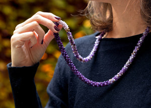 close up of handmade beaded gemstone necklace in shades of purple worn on model