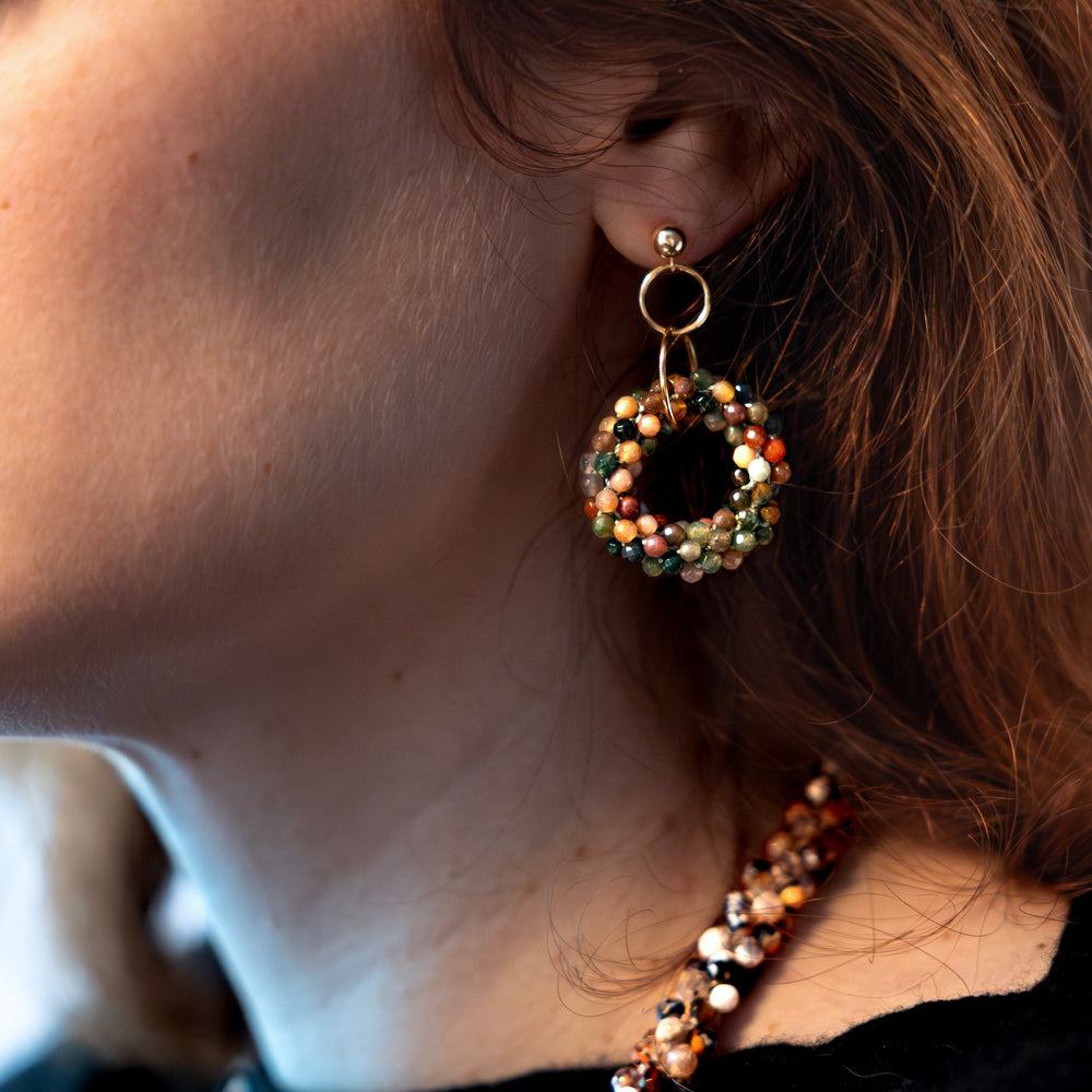 Closeup of handmade beaded gemstone earrings with multicolor agate rings and gold ball post worn on model