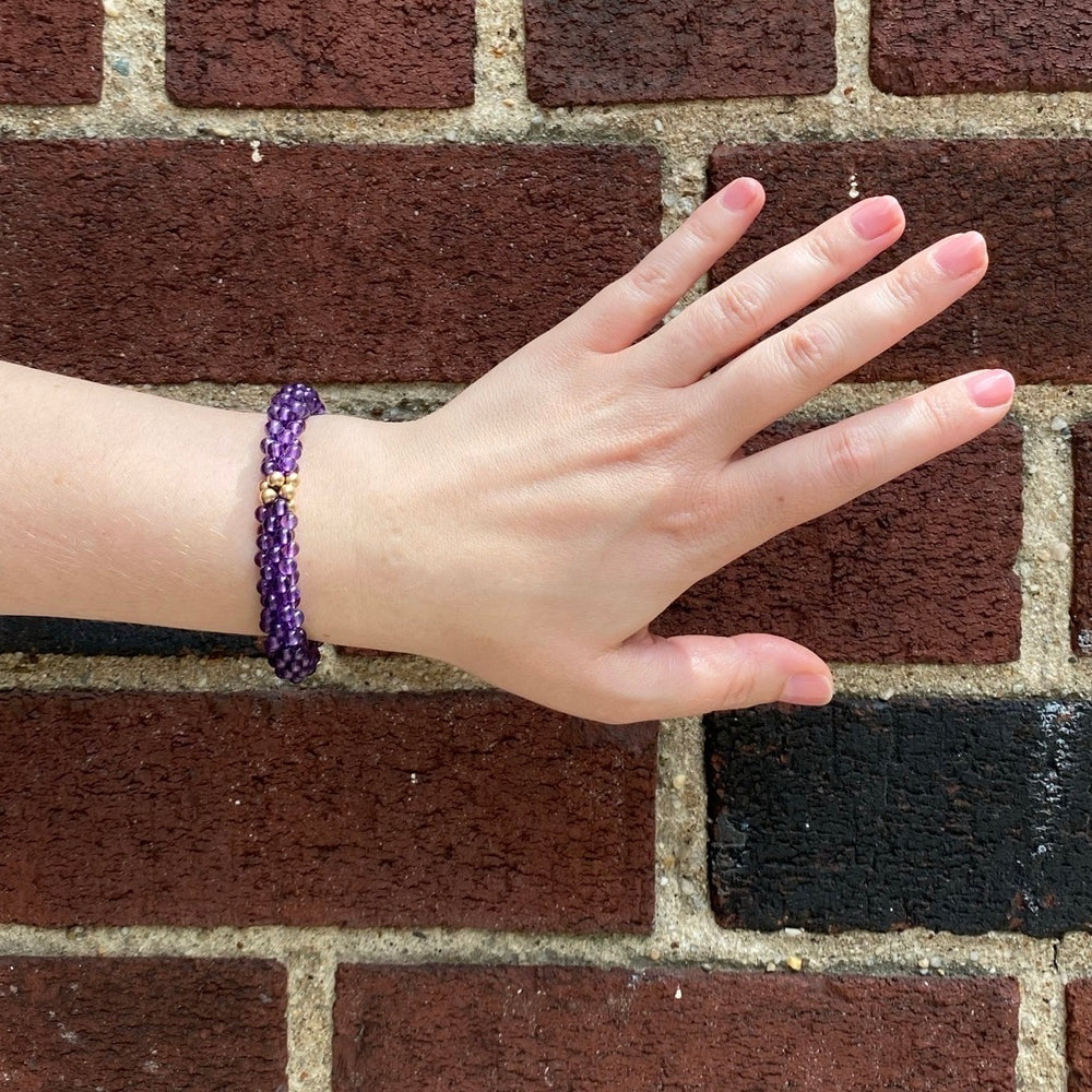 handmade beaded gemstone bracelet in amethyst and gold on model's wrist