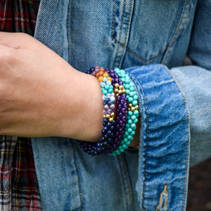 handmade beaded gemstone bracelet in amethyst and gold in a stack on a model's wrist