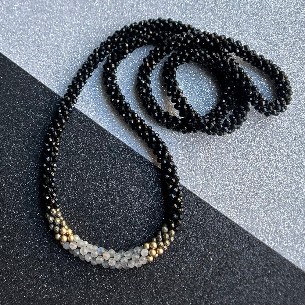 Handmade black beaded necklace with gold and gray accents on a two tone background