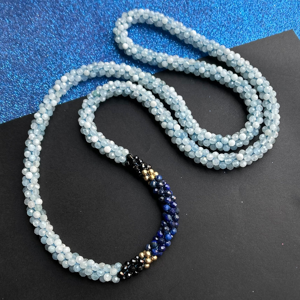Handmade beaded gemstone necklace in shades of blue with black on a two tone background