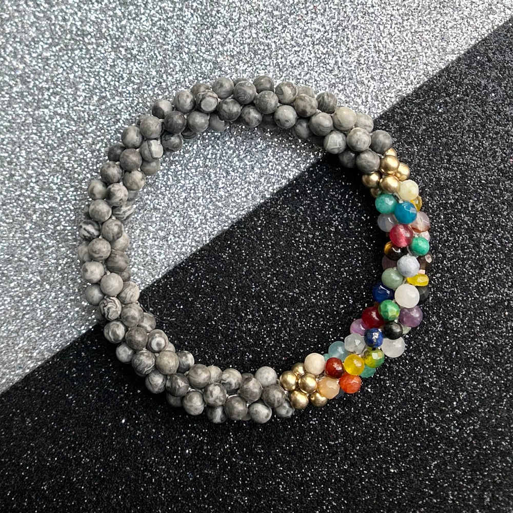 Handmade beaded gemstone bracelet in grey with a multicolor accent on a two tone background