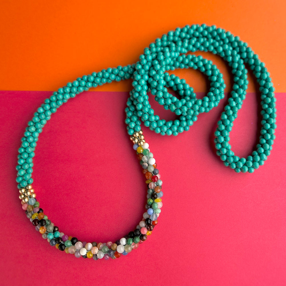Handmade turquoise beaded necklace with multicolored accents on a two-tone background