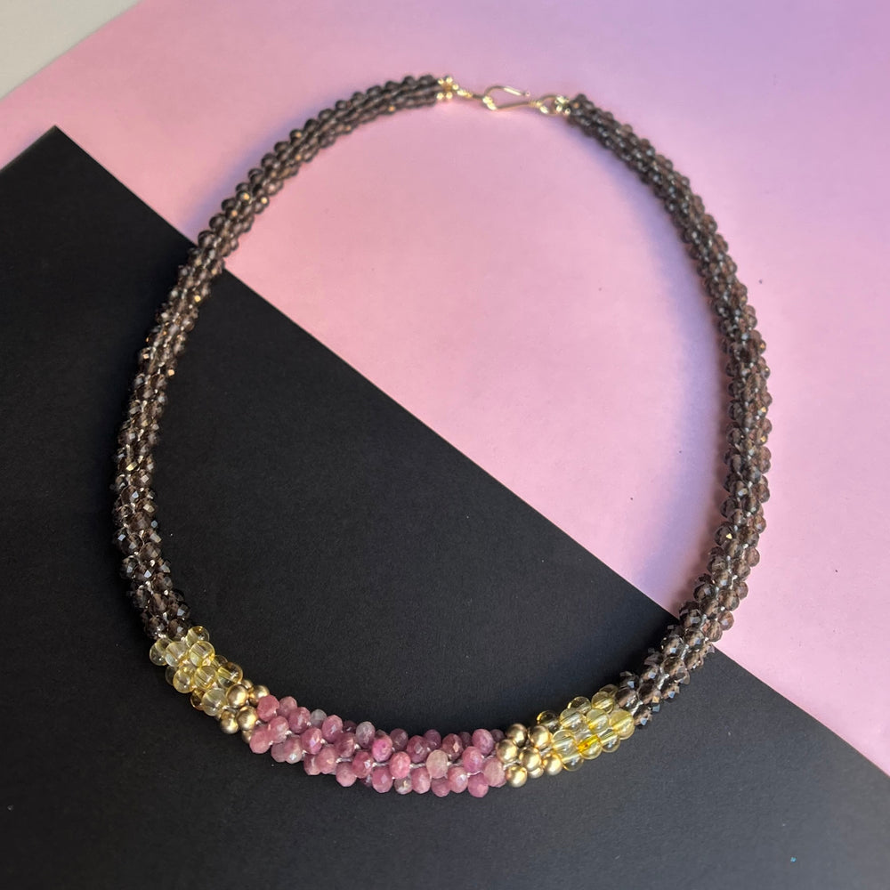 handmade beaded gemstone necklace in brown, yellow and pink with a clasp on a two tone background
