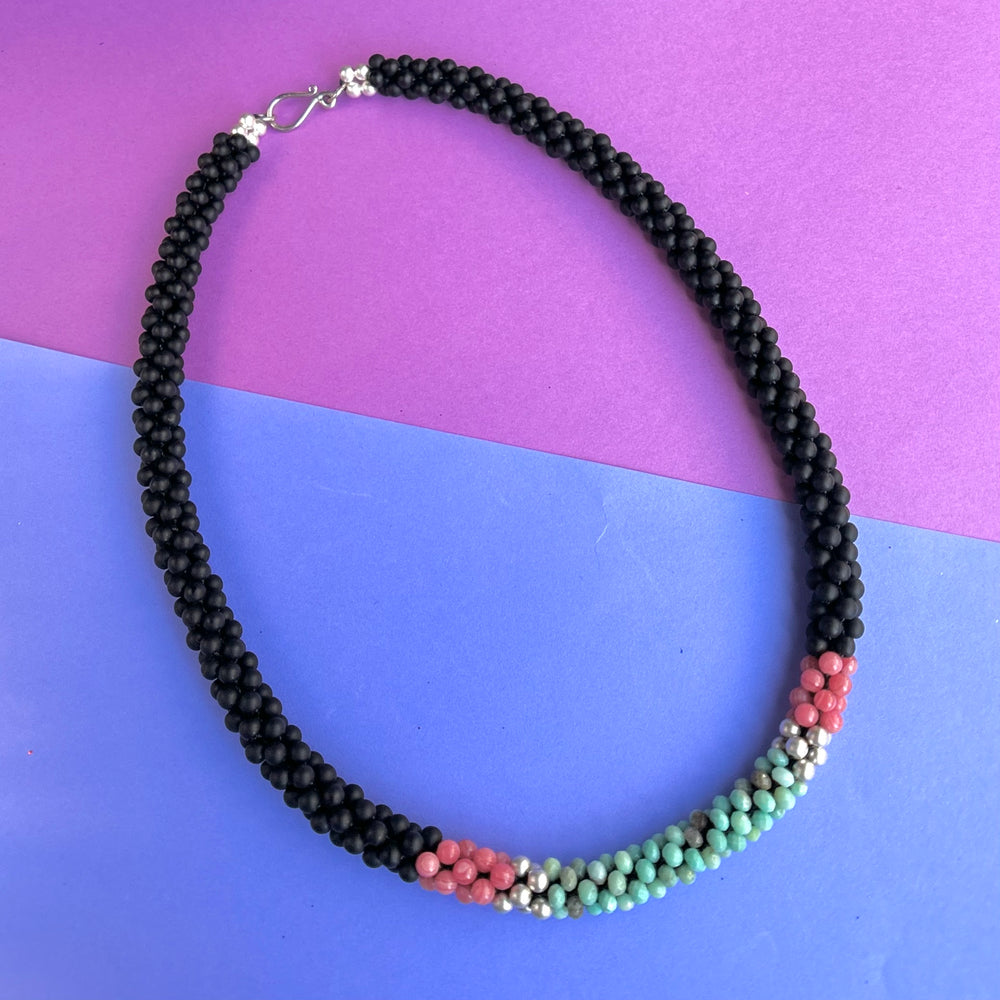 handmade beaded gemstone necklace in black, pink and turquoise with a clasp on a two tone background