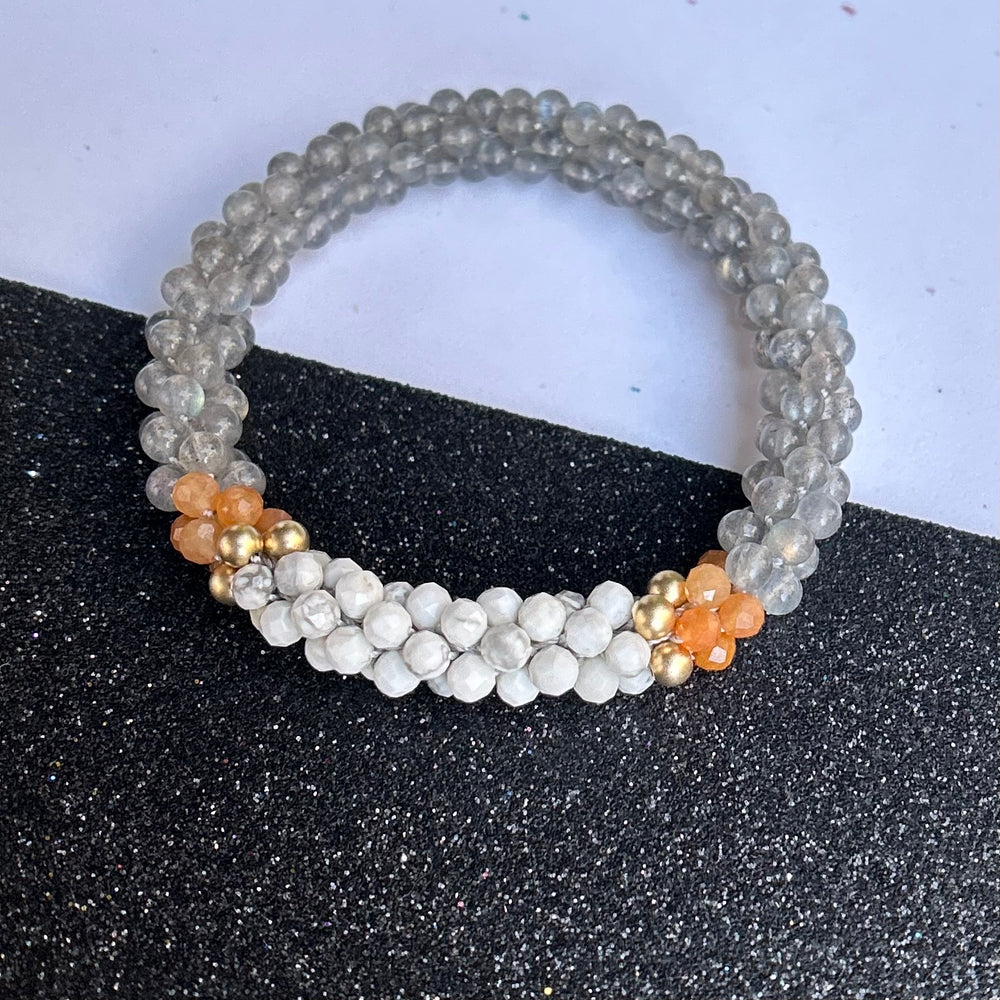 Handmade beaded gemstone bracelet in grey with orange and white accents on a black and white background