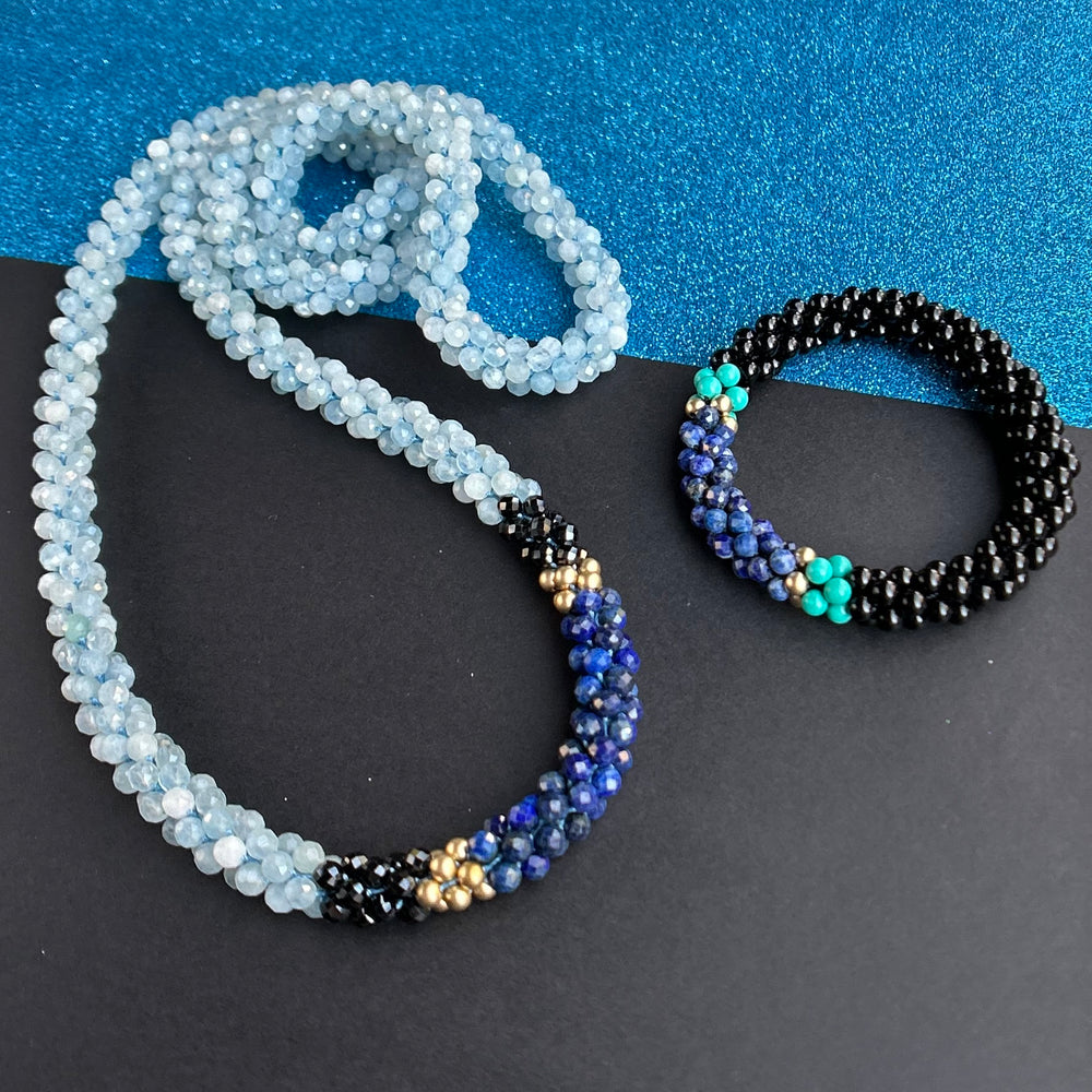 Handmade beaded gemstone bracelet and necklace in black and shades of blue on a two tone background