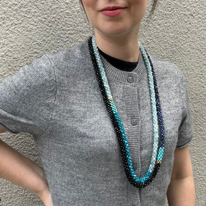 handmade beaded gemstone necklace in aquamarine, apatite, turquoise and gold on model layered with another necklace