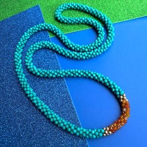 turquoise, carnelian and gold beaded gemstone necklace on blue and green background