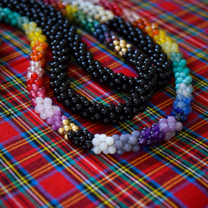 detail of ultimate rainbow and gold beaded necklace with another gemstone necklace on dark background
