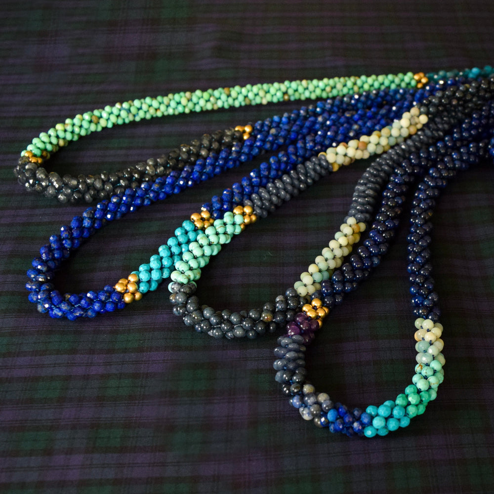shades of blue color block beaded necklace in a group of four gemstone necklaces on dark background