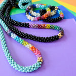 detail of rainbow, turquoise and gold beaded necklace with other rainbow gemstone necklace and bracelets on colorful background