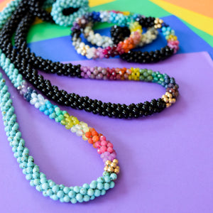 
            
                Load image into Gallery viewer, detail of rainbow, turquoise and gold beaded necklace with other rainbow gemstone necklace and bracelets on colorful background
            
        