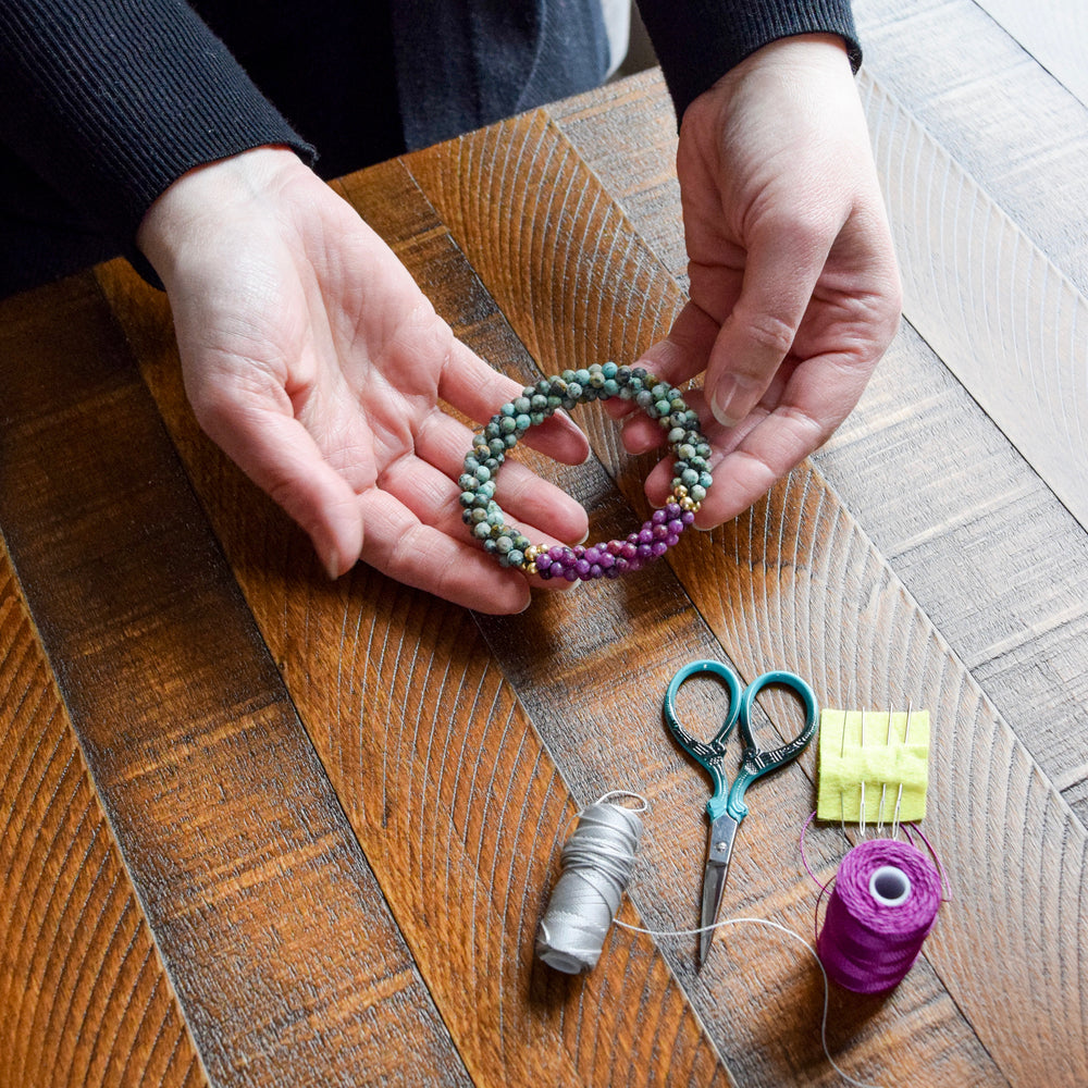 african turquoise and lepidolite bracelet in maker's hands with tools surrounding them